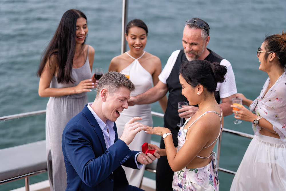 Couple Celebrating Their Engagement On A Boat, Sharing A Joyful Moment Surrounded By Family And Close Friends.